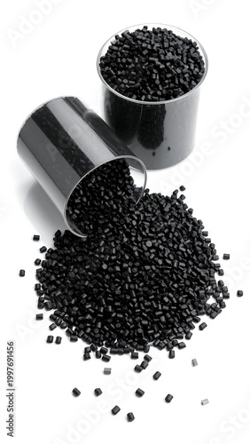 Monochrome shot of plastic granules spilling from a cup, another cup in background. The granules are spread out