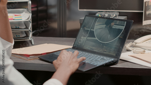 Bild auf Leinwand Policeman studying crime case files on laptop, sitting at desk with detective evidence map on wall