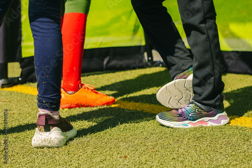 Girls' football players wearing colorful athletic shoes stand on a green artificial turf field, showcasing various footwear styles and vibrant colors in a team setting