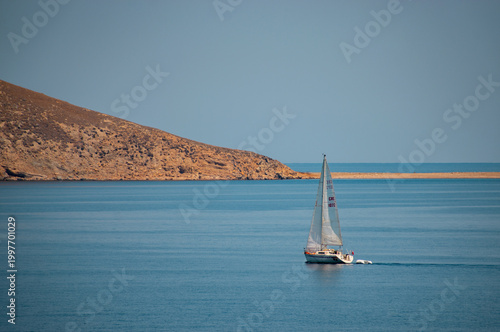 Sailing boat cruising near a rocky coastline under clear blue sky in Greece