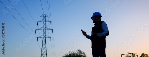 Energy worker in blue hard hat and gilet inspecting power lines infrastructure. Banner - silhouette of a male engineer against a background of high-voltage power transmission line poles. 