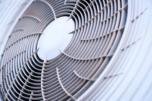 Fascinating abstract geometric pattern created by the circular gray plastic ventilation grille covering the rotating fan blades of a modern outdoor air conditioning unit