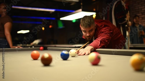 Focused man aiming cue ball playing billiards game in a pool hall bar with friends at night