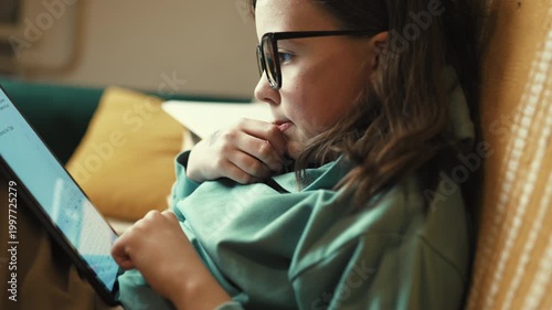 Little Girl in Glasses Using Digital Tablet on Couch with Stack of Books, Child Studying with Pad at Home, 4K 10-bit