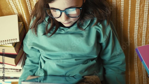 Little Girl in Glasses Using Digital Tablet on Couch with Stack of Books, Child Studying with Pad at Home, 4K 10-bit