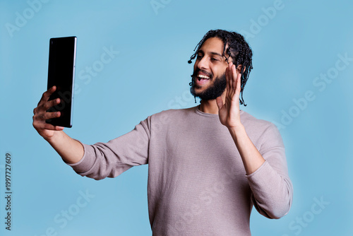 Smiling arab man waving hi during video call on digital tablet using online meeting software app. Cheerful person greeting friend while having virtual communcation in videoconference