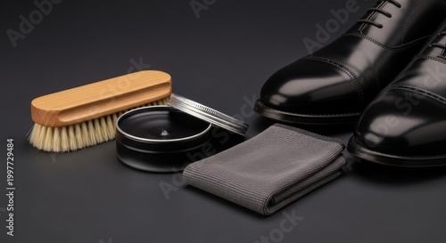 Elegant black leather shoes and a shoe care kit with a wooden brush and polish on a dark background.