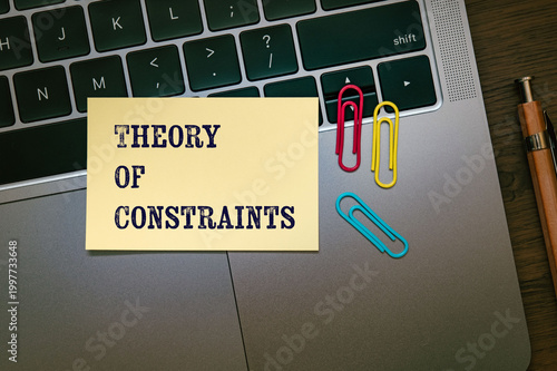Corporate and management concept of Theory Of Constraints represented on sticky note with laptop, clips. Professional business leadership and operations.