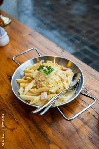 penne pasta are coated in a rich white sauce, tossed with pieces of savory bacon or pancetta, and generously topped with grated parmesan cheese and a fresh sprig of parsley