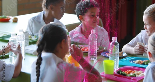 Sharing students wearing light shirts at school lunch table, with trays and water bottles