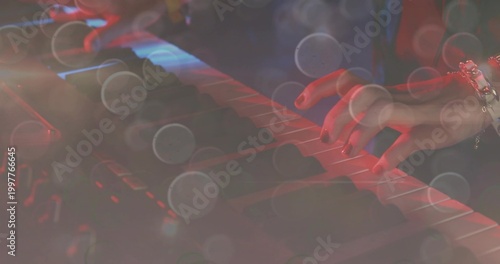 Playing musician's right hand pressing keyboard keys on stage, with dark sleeve, bracelet and bokeh