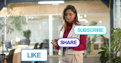 Standing woman wearing maroon top holding phone, checking LIKE SHARE SUBSCRIBE bubbles in office