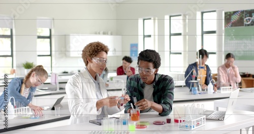 Transferring liquid students in lab coat and goggles working in school lab with beaker, test tubes