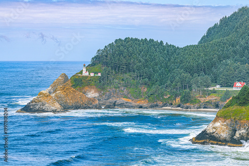 Φωτογραφία Heceta Head Lighthouse stands on a forested headland above the Pacific Ocean, with a coastal highway visible along the rugged Oregon shoreline