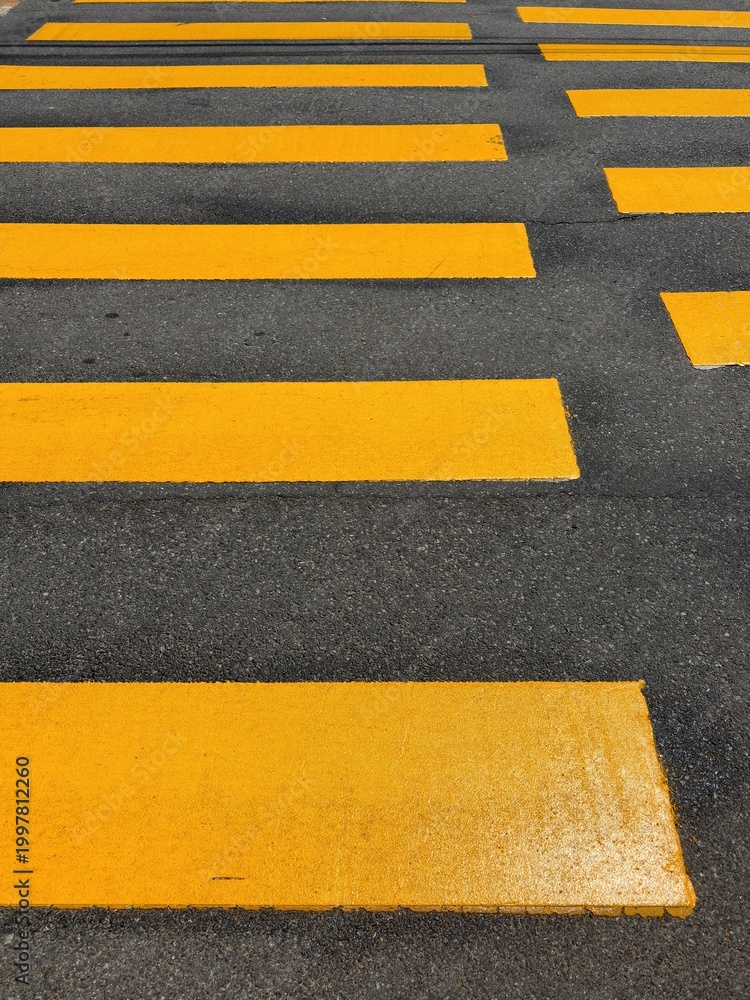 Fototapeta premium Top view of vibrant yellow pedestrian crosswalk patterns on dark asphalt street
