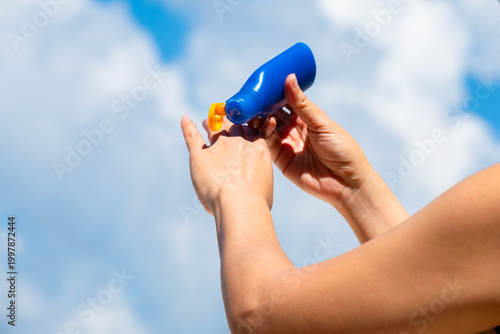 Sunscreen from blue bottle on palm she apply hand and arm with bright sun and blue sky background, skin protection and summer skincare concept	