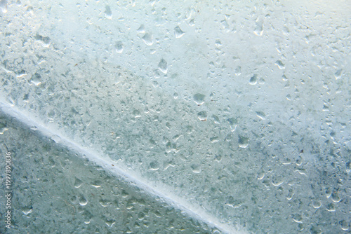 A captivating macro photograph featuring natural morning dew droplets and condensation collected on the surface of a sheet of clear plastic. The image captures the foggy effect created by countless sm