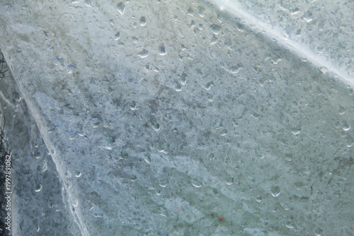 A captivating macro photograph featuring natural morning dew droplets and condensation collected on the surface of a sheet of clear plastic. The image captures the foggy effect created by countless sm