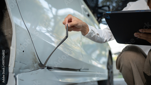 Cuadro en lienzo Close-up of inspector using tablet and measuring tool to assess dent and damage on white car door during vehicle appraisal or insurance claim
