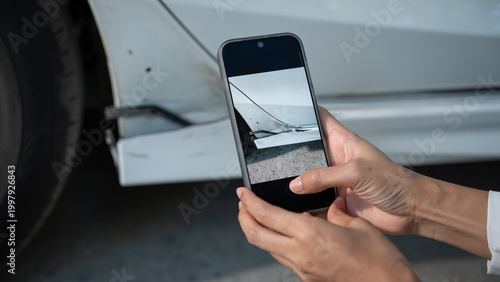 Fotografi Hands holding smartphone photographing dent and scratch on car body near wheel, documenting vehicle damage for insurance claim or repair