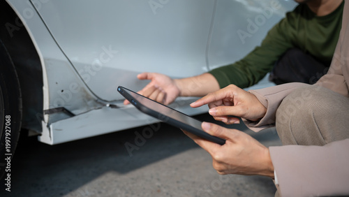 Obraz na płótnie Close-up of people inspecting car body damage using a tablet beside a vehicle, suggesting auto repair assessment, insurance claim, and roadside assistance