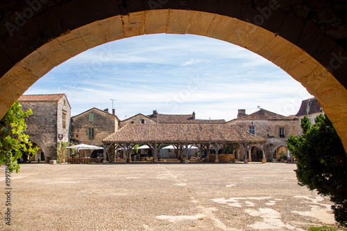 View of Monpazier medieval square framed by a historic stone arch