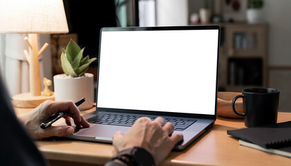 Laptop mockup on wooden desk with blank white screen, hands typing, cozy home office workspace.