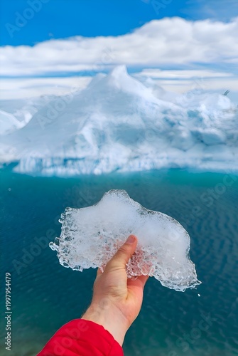 Hand holding glacier ice with a massive iceberg and blue ocean in the background.