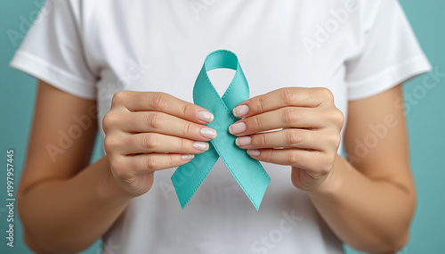 Close up of a woman holding a teal awareness ribbon to support ovarian cancer and sexual assault awareness month