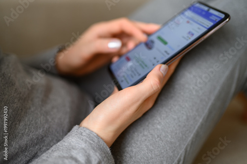 Woman sitting on sofa at home, looking at information about cars on mobile phone, close-up. Girl looking at information about car rental on car rental website on phone.