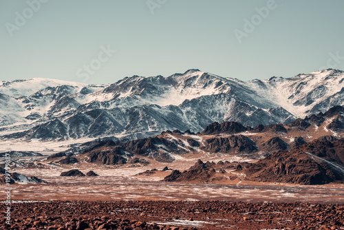 Schilderij op canvas Vast Snow-Capped Peaks Rise Over Rocky Terrain in Southern Mongolia