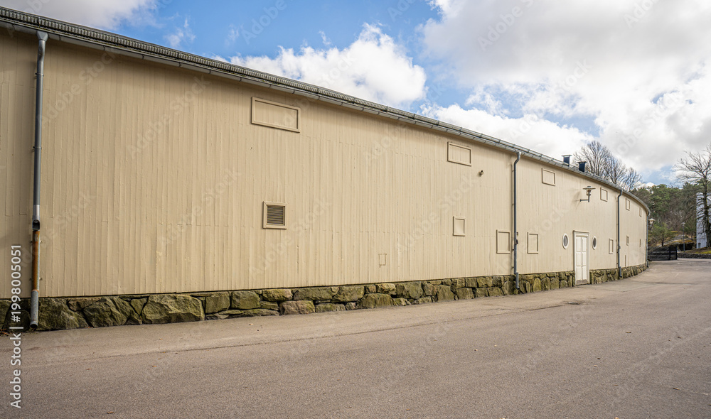 Fototapeta premium Long industrial warehouse building exterior with minimal windows and paved empty surroundings.