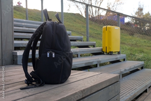 Fotografía Black Backpack And Yellow Suitcase On Steps, Backpack Leaning Against Wooden Sta