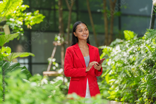 Young Asian Woman holding smartphone outdoors in a tropical garden