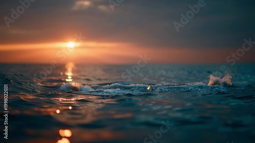 A whale tail emerges from the ocean at sunset with water dripping and the sun glowing on the horizon.