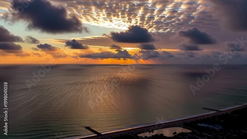 Aerial tracking slow motion pan of airplane wing over ocean with sun reflecting on water along coastal shoreline at sunset