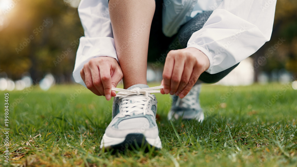 Obraz premium Person, hands and tying with shoes on grass field for fitness, workout preparation or run in nature. Active, runner or getting ready with sneakers or laces for outdoor exercise or training in park