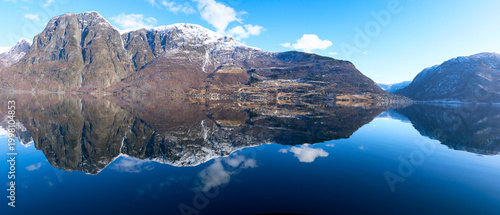 Panoramic view of majestic snow-capped mountains perfectly reflected in a calm blue fjord