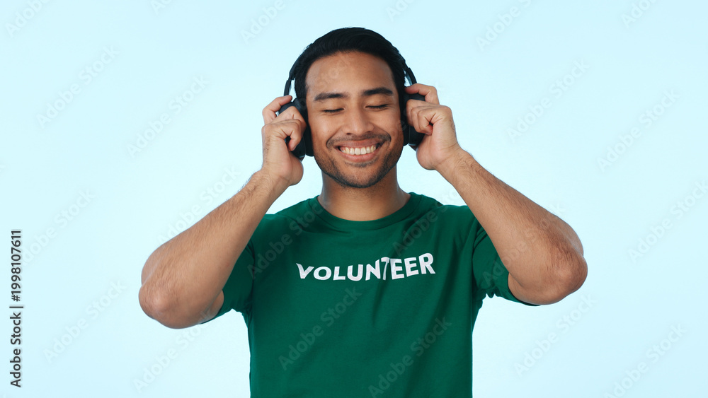 Fototapeta premium Studio, volunteer and man with headphones, charity and listening to music with subscription on break. Blue background, humanitarian and happy person with tech for playlist, ngo and streaming audio