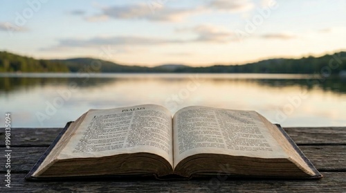 Photos Open Holy Bible displaying the book of Jeremiah, resting on a rustic wooden dock by a peaceful lake at sunset