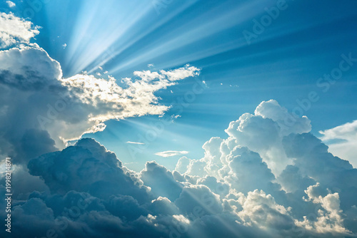 Sunbeams shining through fluffy white clouds in blue sky