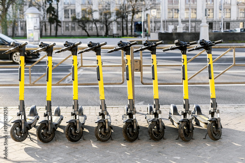Electric scooters parked in a row on urban sidewalk, sustainable transport concept.