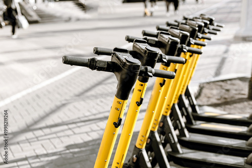 Yellow electric scooters lined up in city street, urban eco transport concept.