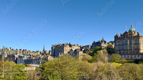 Historic Edinburgh Old Town skyline viewed across Princes Street Gardens under blue skies, Scotland. 
