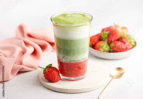 Layered strawberry matcha latte in glass with milk on minimal background, selective focus
