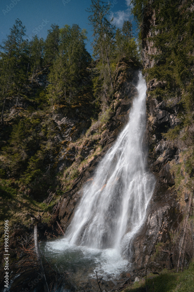 Obraz premium Powerful waterfall cascading down a rocky forest cliff in an alpine landscape in Tyrol, Austria.