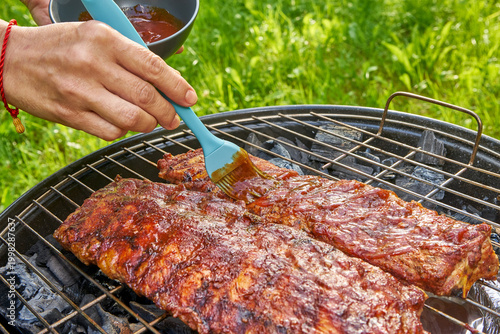 Grilled ribs celebration. Preparing and basting juicy pork ribs during relaxed outdoor summer barbecue