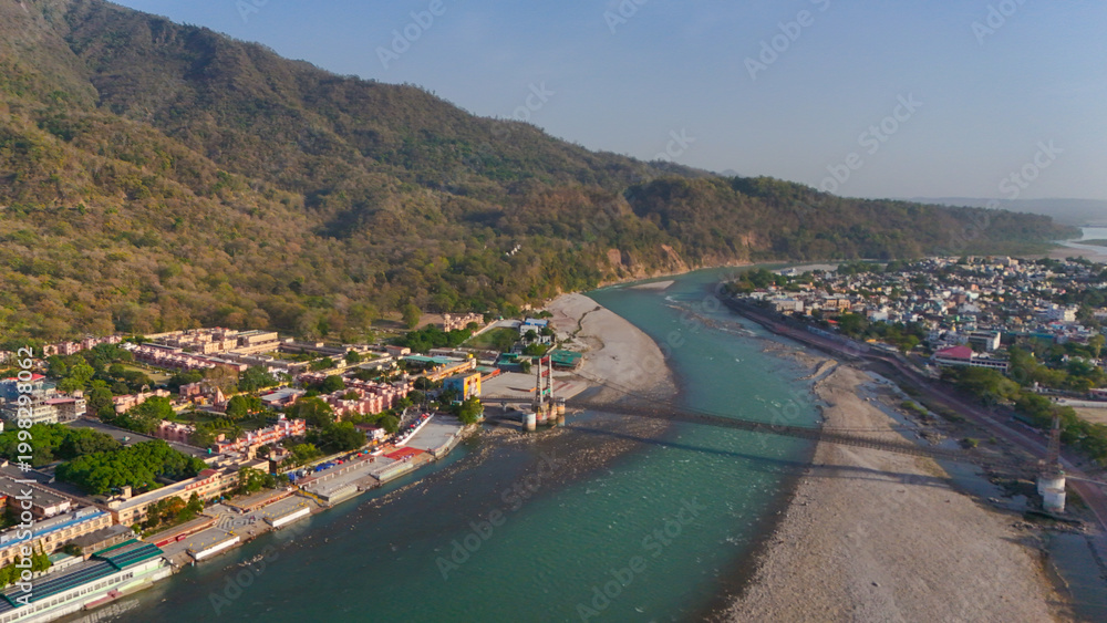 Fototapeta premium Stunning top view drone shot capturing Rishikesh with the flowing Ganga river, iconic bridges, and lush green mountains.