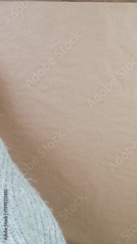 Close-up of a sweater-clad hand unrolling a roll of kraft paper on a wooden table and folding back the edge.
