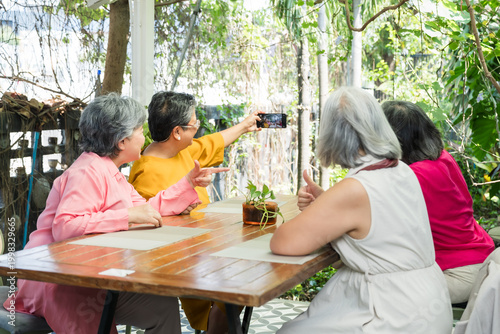 Obraz na plátně Group of senior Asian women gather at outdoor cafe, stretching smartphone for reunion selfie after long separation, celebrating friendship, cheerful brunch moment, later life connection, happy memory